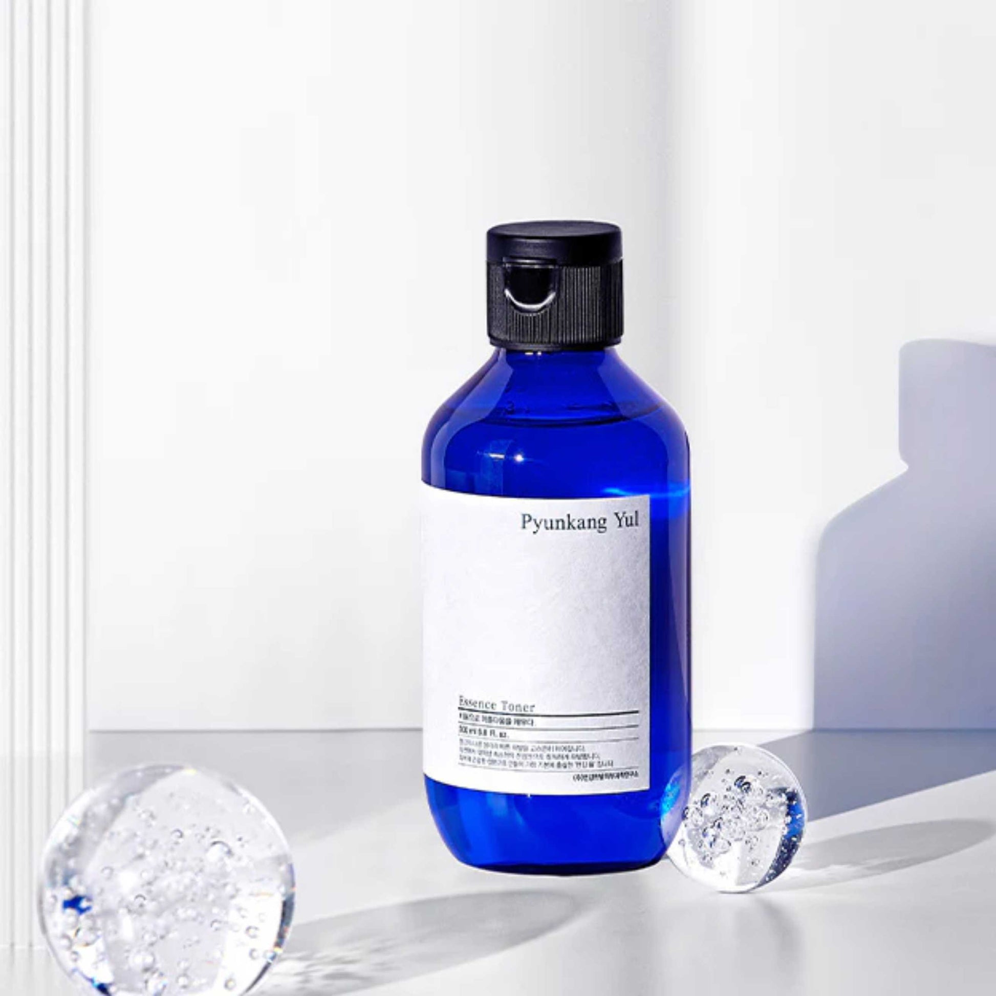 Pyunkang Yul Essence Toner i blå flaske med isbiter på hvit bakgrunn